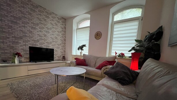 A living room with a brick wall, a flat-screen TV, a sofa, a coffee table, and a potted plant. - A central, cozy family retreat for 4 people—perfect for short getaways (Bremerhaven)