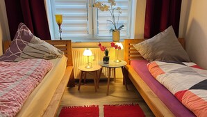 A cozy room with two wooden beds, a small table with a lamp, a red rug, and a window with curtains and flowers. - A central, cozy family retreat for 4 people—perfect for short getaways (Bremerhaven)