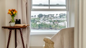 A room with a view of a coastal town, a small table with a vase of flowers, and a chair with a patterned cushion.