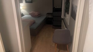 Een kleine kamer met een bed, een stoel, een tafeltje en een kledingkast.