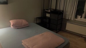 Een kamer met een bed, een klein zwart opbergmeubel, een radiator en een raam met gordijnen.