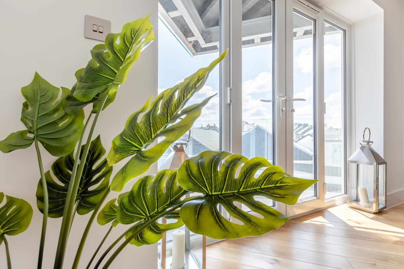 Apartamento moderno com grandes janelas, piso de madeira e plantas tropicais.