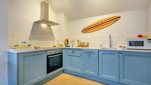 Une cuisine avec des armoires bleues, une hotte de cuisinière en acier inoxydable, un four à micro-ondes et une décoration murale représentant une planche de surf.