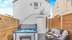 Un bain à remous dans un jardin, avec un escalier menant à un deuxième étage, un canapé en osier et une clôture en bois.