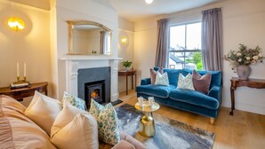 A living room with a fireplace, a blue sofa, and a large mirror. - 6 Bed in Abersoch (oc-c29569) (Abersoch)