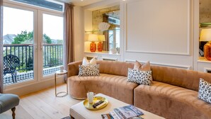 A modern living room with a brown sofa, two leopard print cushions, a coffee table with a remote and magazines, and a large window with a view of the outdoors. - 6 Bed in Abersoch (oc-c29569) (Abersoch)