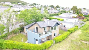 A modern two-story house with a balcony, surrounded by well-maintained hedges and a grassy lawn. - 3 Bed in Mynytho (oc-m29517) (Mynytho)