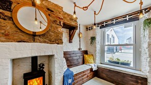 A cozy room with a fireplace, wooden bench, and a large window with a view of the street. - 2 Bed in Looe (oc-a29612) (Looe)