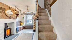 A cozy interior with a fireplace, a wooden staircase, and a view of the outside. - 2 Bed in Looe (oc-a29612) (Looe)