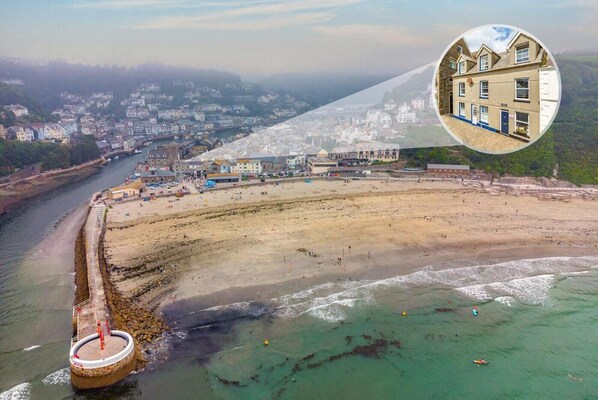 An aerial view of a coastal town with a sandy beach, a river, and a large building with a blue door. - 2 Bed in Looe (oc-a29612) (Looe)