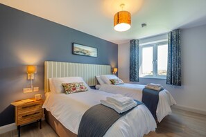 Een tweepersoonskamer met twee bedden, een raam met gordijnen, een schilderij aan de muur en een nachtkastje met een lamp.