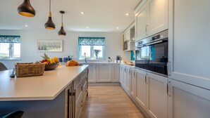 A modern kitchen with white cabinets, a large island, and pendant lighting. - 5 Bed in Aberdaron (oc-b29652) (Anelog)