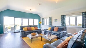 A spacious living room with two sofas, a coffee table, and a large window offering a view of the outdoors. - 5 Bed in Aberdaron (oc-b29652) (Anelog)
