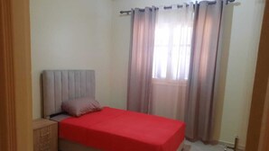 Une chambre à coucher avec un lit, une table de chevet, une armoire en bois et une fenêtre avec des rideaux.