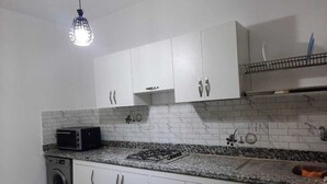 Une cuisine compacte avec des meubles blancs, une cuisinière à gaz, un lave-linge et un four à micro-ondes.