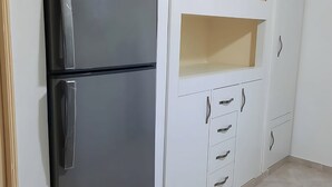 Une cuisine avec un réfrigérateur noir, des armoires blanches et un sol carrelé.