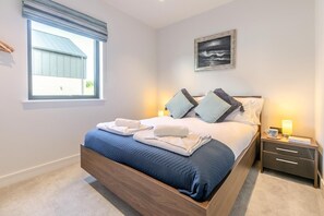 A bedroom with a bed, bedside tables, a window, and a painting on the wall. - 4 Bed in Littleham (oc-h29753) (Littleham)