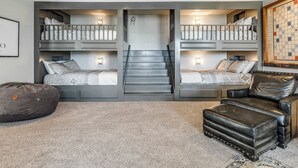 A room with bunk beds, a staircase, a bean bag, and a leather ottoman. - MoonBeam Landing, Boardwalk Luxury Steps from Pool, Shops & Lake Fun (Eufaula)