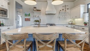 A spacious kitchen with a large island, pendant lighting, and wooden chairs. - MoonBeam Landing, Boardwalk Luxury Steps from Pool, Shops & Lake Fun (Eufaula)