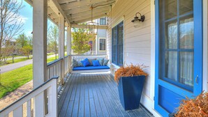 A covered porch with a blue bench, a planter with dried plants, and a blue door. - MoonBeam Landing, Boardwalk Luxury Steps from Pool, Shops & Lake Fun (Eufaula)