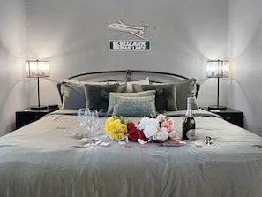 A neatly made bed with a bouquet of flowers, a bottle of champagne, and a decorative airplane sign on the wall. - 692 Walk-in Lakefront Oasis - Cozy, Calm, Scenic (Branson)