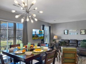 A modern living room with a dining area, a large window, and a television displaying a scenic view. - 692 Walk-in Lakefront Oasis - Cozy, Calm, Scenic (Branson)