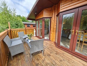 A wooden deck with wicker furniture and a glass door leading to an outdoor area.
