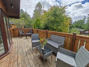 Eine Terrass mit Glastür, die zu einem Raum führt, möbliert mit Korbstühlen und einem Tisch mit Blumen in einer Vase.