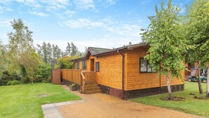 A wooden cabin with a brick pathway leading to the entrance, surrounded by trees and a grassy yard.