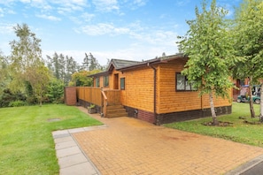 Eine Holz-Blockhütte mit einem Ziegelweg, der zum Eingang führt, umgeben von Bäumen und einem Rasen.