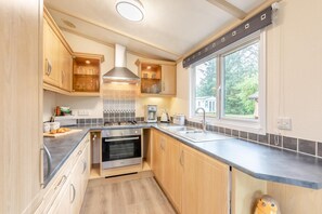A modern kitchen with wooden cabinets, a built-in oven, a stainless steel sink, and a window providing a view of the outdoors.