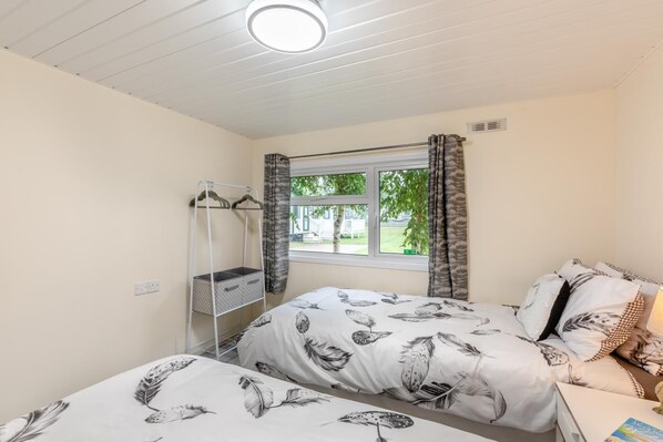 A bedroom with two beds, a window with curtains, a bedside table, and a hanging storage unit.