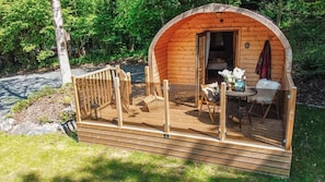 A wooden cabin with a porch, a bed, and a dining area.