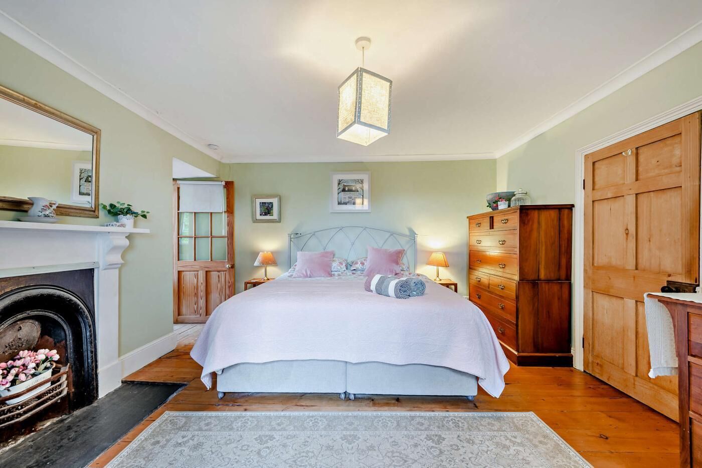 A bedroom with a bed, a dresser, a mirror, a fireplace, and a chandelier.