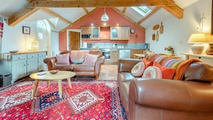 Ein geräumiger Loft mit hohen Decken, freiliegenden Holzbalken, einer gemütlichen Wohnbereits mit Ledersofas und einem gemusterten Teppich sowie einer Küche mit modernen Geräten.