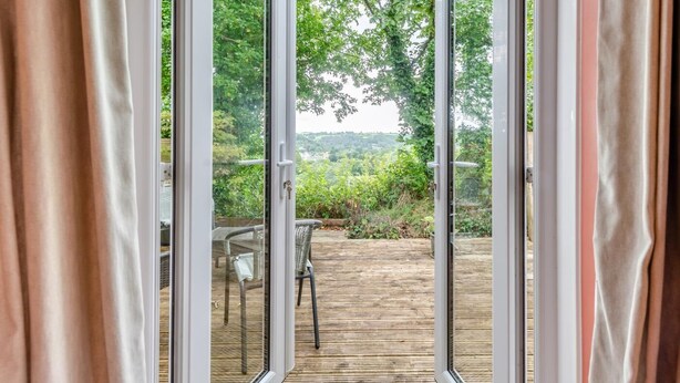 Blick durch eine Glastür auf eine Terrasse mit Holzdeck, Tisch und Stühlen.