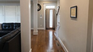 A hallway with wooden flooring, a black leather couch, a clock, and a framed picture on the wall. - Near Downtown and Midtown, Quiet Cul-de-sac Decatur Home with Deck & Balcony, (Decatur)