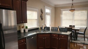 A kitchen with dark wooden cabinets, a stainless steel refrigerator, a granite countertop, a built-in dishwasher, and a dining area with a table and chairs. - Near Downtown and Midtown, Quiet Cul-de-sac Decatur Home with Deck & Balcony, (Decatur)