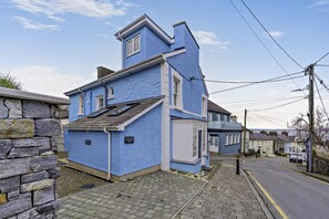 Ein blaues Haus mit Mauerwerk, einem gepflasterten Auffahrt und einem wolkenlosen Himmel.