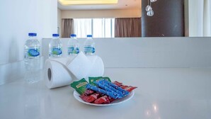 Ett hotellrum med ett vitt bord, tre flaskor vatten, en toalettpappersrulle och en tallrik med snacks.