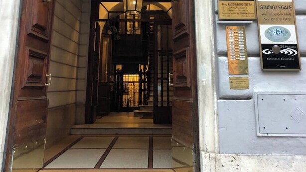 An entrance with a wooden door and a metal gate, leading to a corridor with a hanging light fixture. Plaques are mounted on the wall to the right. - NEW! Nice apartment 2 steps from villa Borghese and Spanish Steps (Roma)
