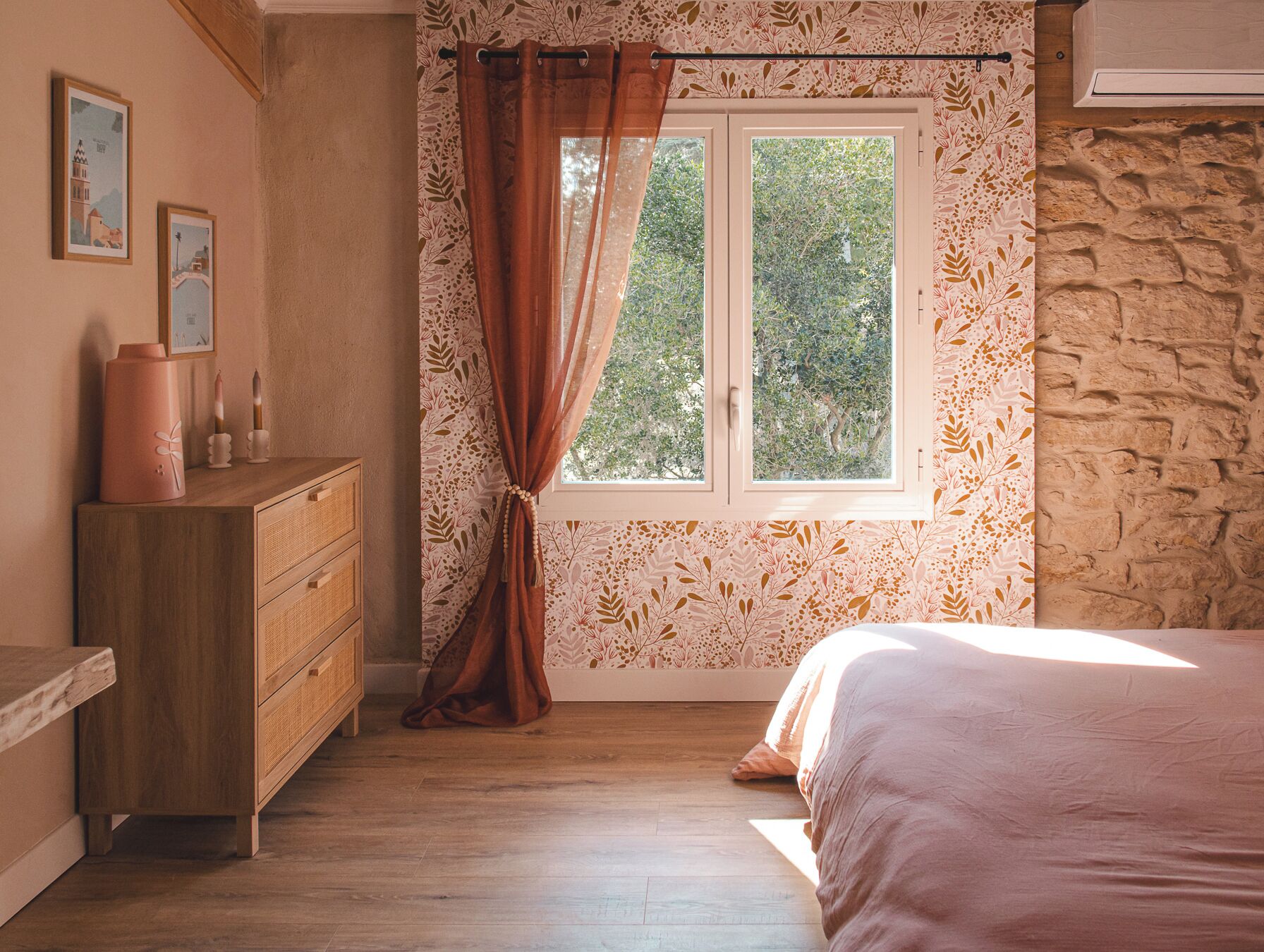 Quarto com cômoda de madeira, uma cama, janela com cortina e parede com padrão de folha.
