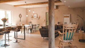 Een ruime woonkamer met een houten schommelstoel, een eettafel met stoelen en een bank.
