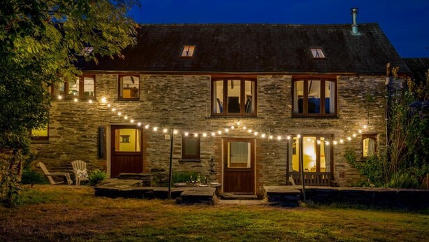 A stone house with a well-lit front porch, a small deck, and a string of lights. - 4 Bed in Hebron (oc-y30097) (Whitland)