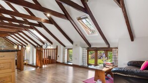 A spacious loft with exposed wooden beams, a skylight, a wooden dining table, and a leather sofa. - 4 Bed in Hebron (oc-y30097) (Whitland)