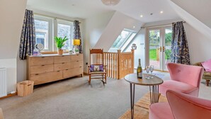 A cozy room with a wooden dresser, a chair, a pink sofa, and a small table with a bottle and glasses. - 1 Bed in Strathpeffer (oc-h30077) (Strathpeffer)