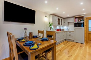 A dining area with a wooden table set for four, white cabinets, a built-in oven, and a flat-screen TV mounted on the wall. - 1 Bed in Strathpeffer (oc-h30077) (Strathpeffer)