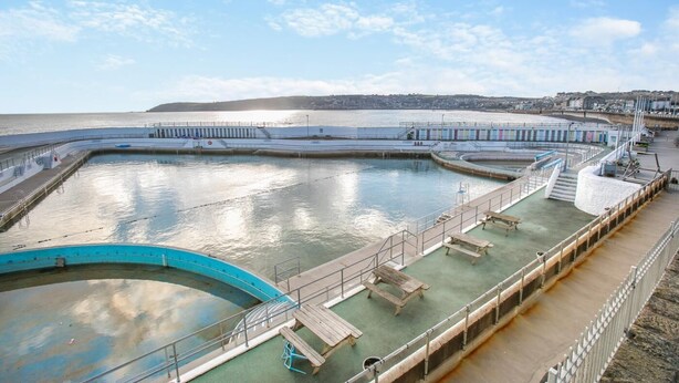 A large, rectangular swimming pool with a surrounding walkway, connected to a pier extending into the water. - 2 Bed in Penzance (oc-g30154) (Penzance)