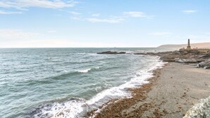A coastal beach with a rocky shoreline, waves, and a monument. - 2 Bed in Penzance (oc-g30154) (Penzance)