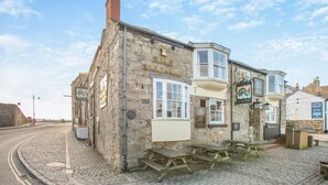 A stone building with a corner window, a sign for 'St. Austell's', and a wooden bench outside. - 2 Bed in Penzance (oc-g30154) (Penzance)